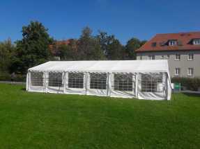Partyzelt mieten Ein großes weißes Zelt steht auf einer grünen Wiese, umgeben von Bäumen und Häusern.