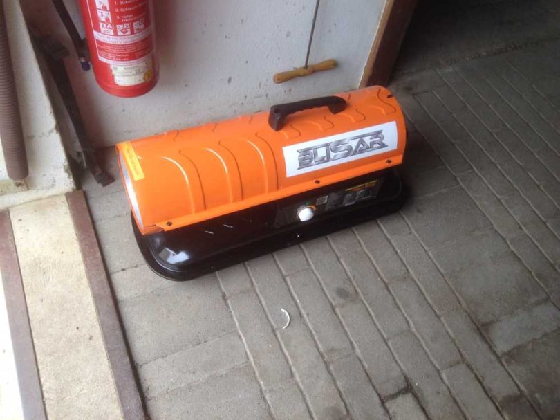 Oranger Heizkörper mit schwarzem Unterteil auf einem Holzboden.