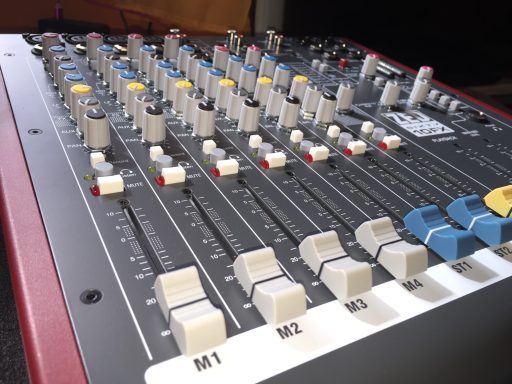 Mischpult mit Reglern, Schaltern und farbigen Tasten für Audioanpassungen.