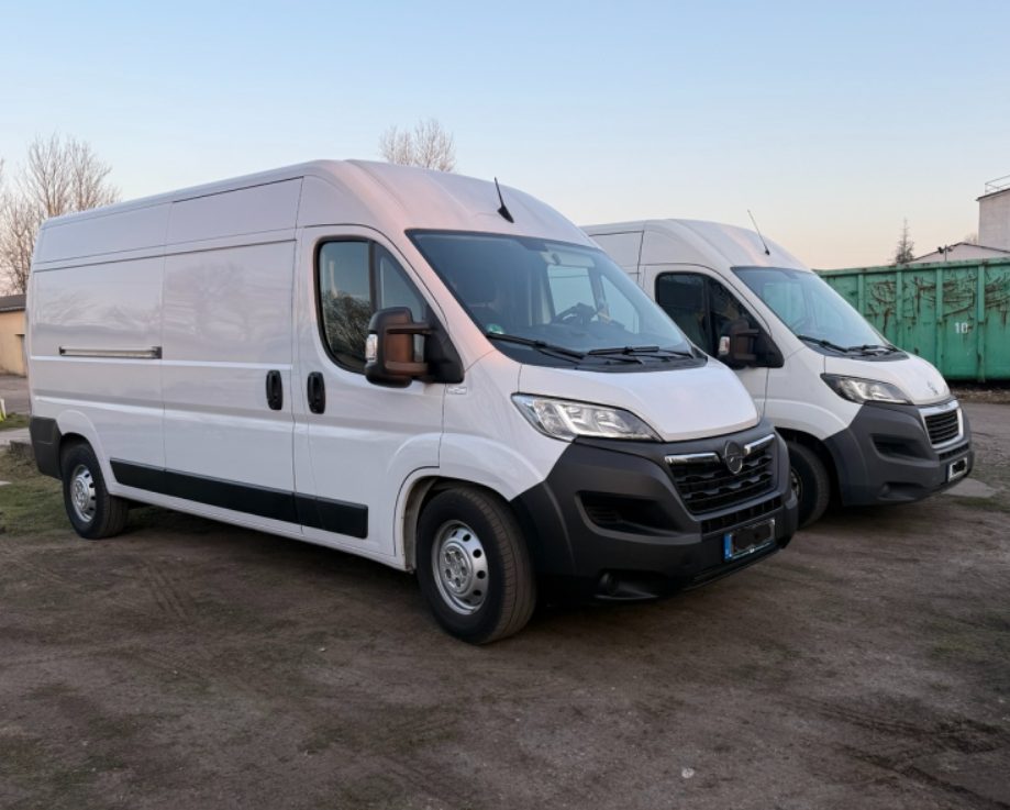Drei weiße Lieferwagen stehen auf einem Parkplatz vor bewölktem Himmel.