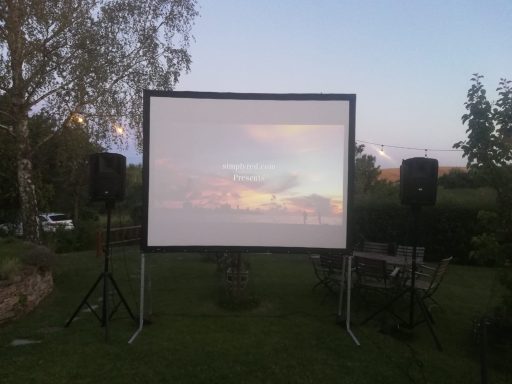 Projektionsleinwand im Freien, mit Lautsprechern und Sonnenuntergang im Hintergrund.