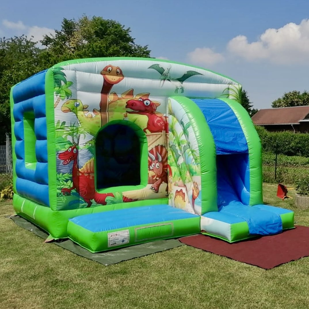 Bunte Hüpfburg mit Dinosaurier-Motiv auf grünem Gelände.