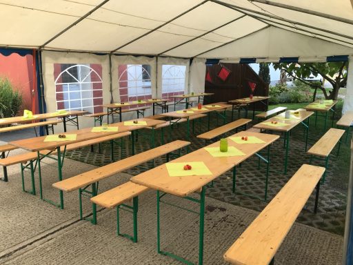 Bierzeltgarnitur mieten Biertische und Bänke in einem Zelt, gedeckt mit grünen Servietten und einer Blume.