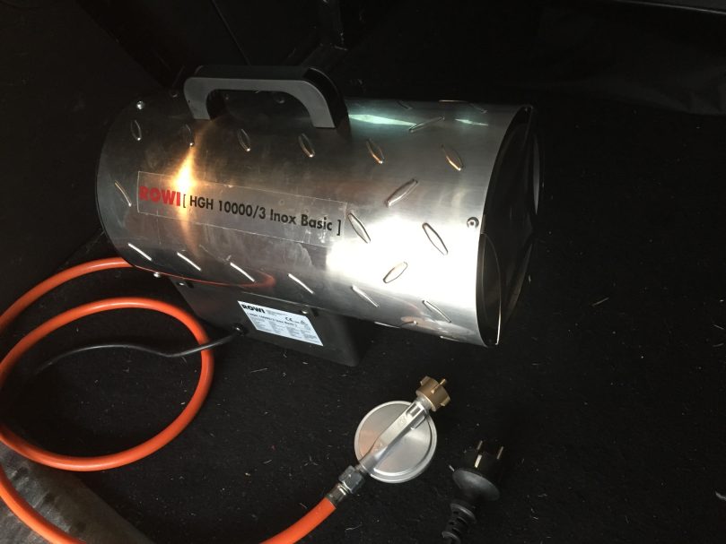 Ein tragbarer Heizstrahler mit Metallgehäuse und Schlauchanschluss.