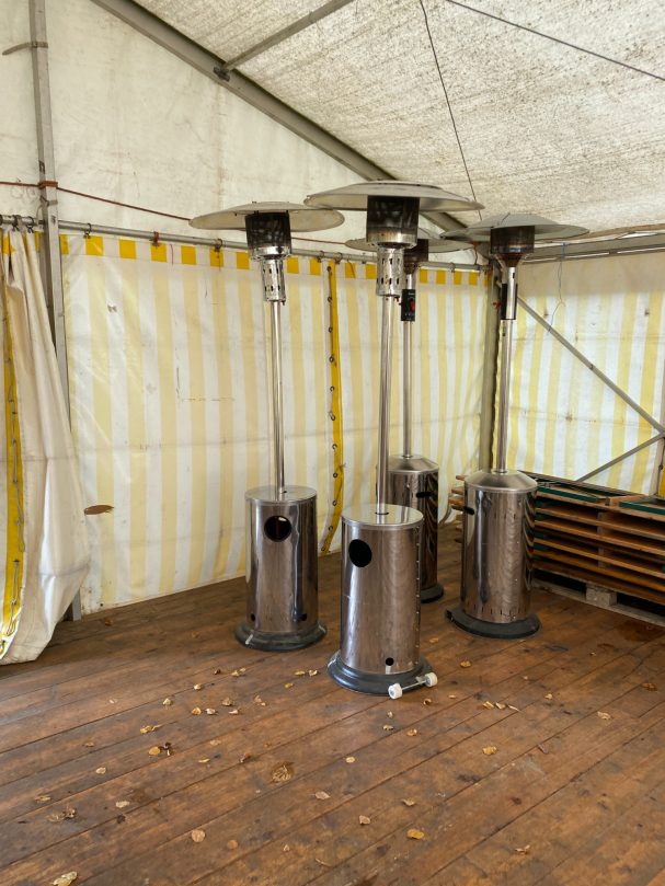 Vier stehende Heizstrahler in einem Zelt mit gestreifter Wand.