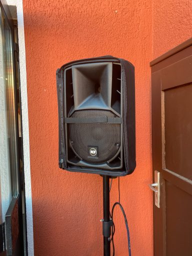 Lautsprecher auf einem Stativ vor einer rötlichen Wand.