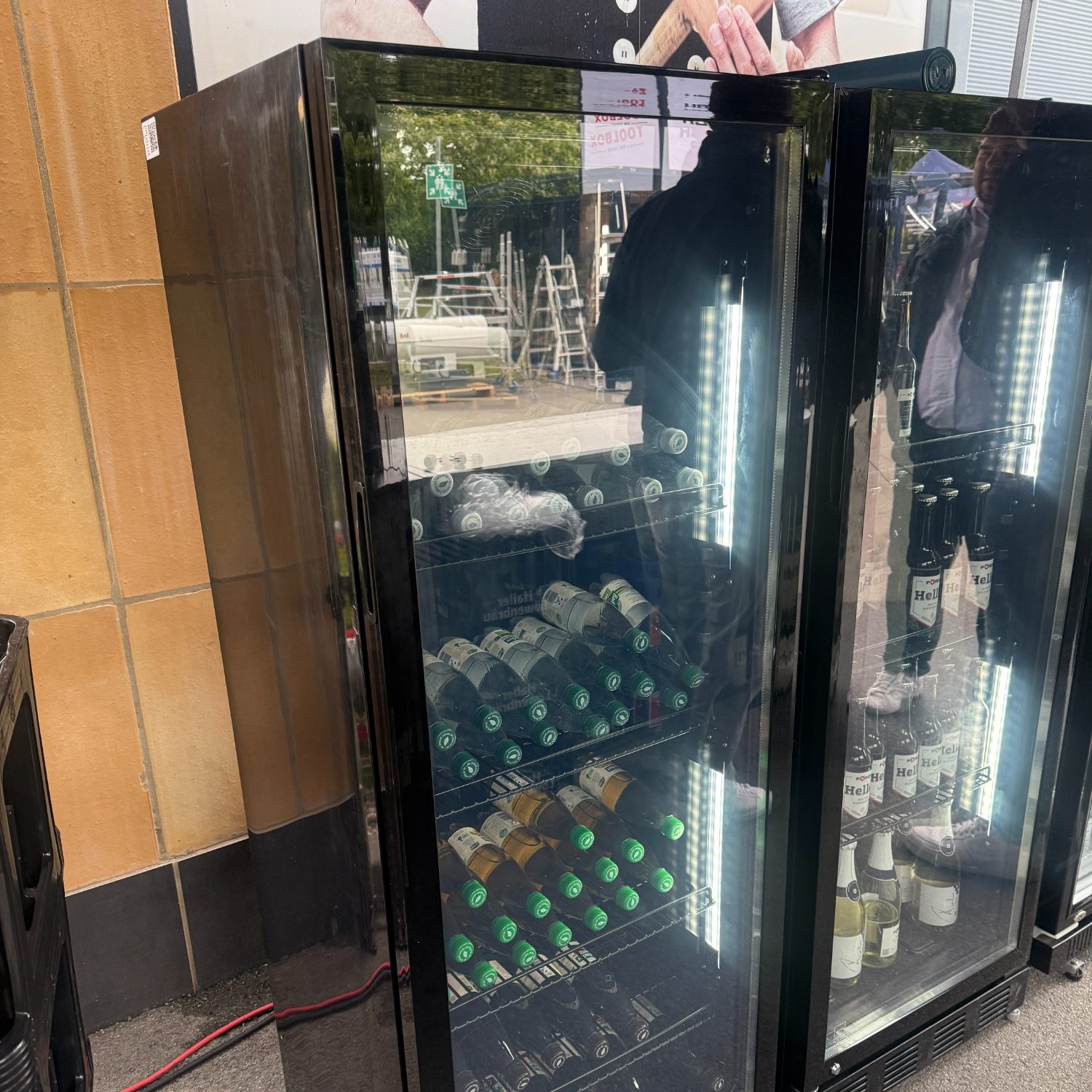 Schwarzer Kühlschrank mit beleuchteten Regalen, gefüllt mit Getränken und Flaschen.